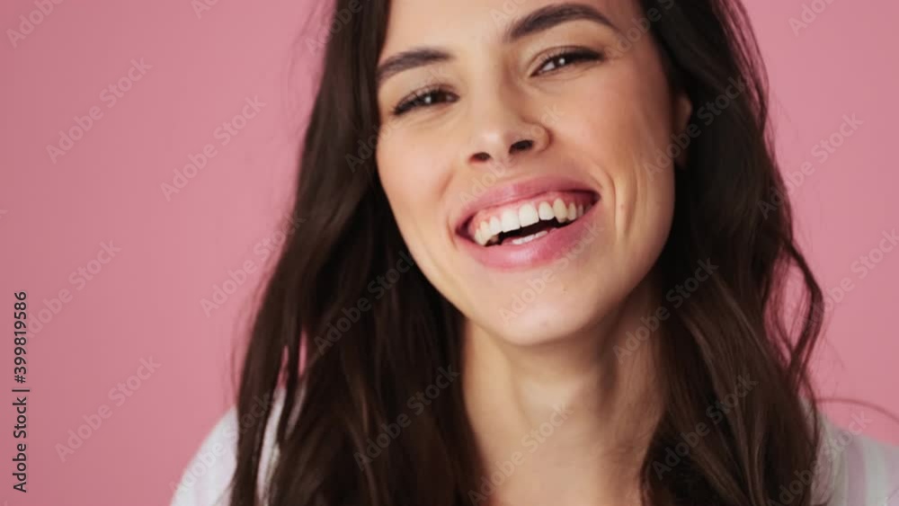 A close-up view of a cheerful young woman is posing to the camera standing isolated over a pink background in the studio A close-up view of a cheerful young woman is posing to the camera standing isolated over a pink background in the studio