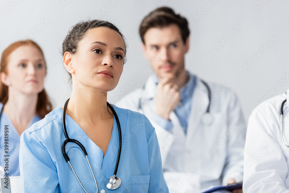 African american nurse looking away during meeting with blurred colleagues on background African american nurse looking away during meeting with blurred colleagues on background