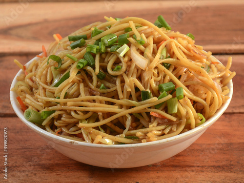 Veg Hakka Noodles a popular oriental dish made with noodles and vegetables, served over a rustic wooden background, selective focus photo