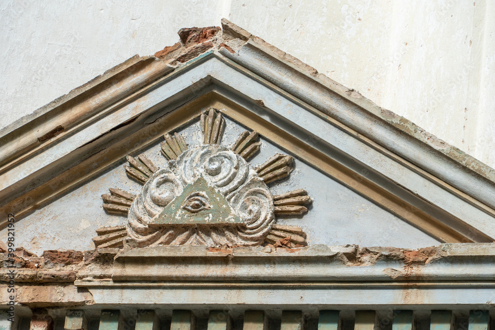 Masonic symbol on the wall of an ancient dilapidated church. The eye of God in the center of the pyramid rises above the mortal worlds in the rays of the rising sun and shrouded in a haze clouds. Masonic symbol on the wall of an ancient dilapidated church. The eye of God in the center of the pyramid rises above the mortal worlds in the rays of the rising sun and shrouded in a haze clouds.