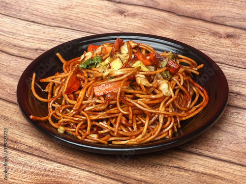 Schezwan Veg Noodles a popular indo-chinese dish made with noodles, vegetables and schezwan sauce, served over a rustic wooden background, selective focus