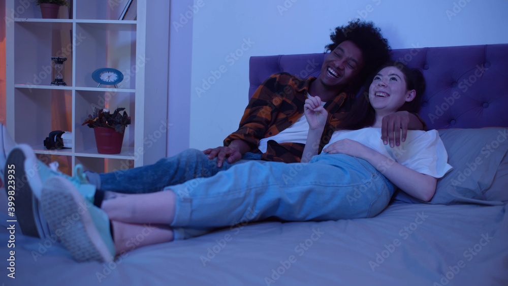 Obraz premium Laughing multiethnic family watching movie together at home in evening