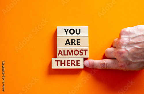 You are almost there symbol. Wooden blocks form the words 'You are almost there' on beautiful orange background. Male hand. Business and you are almost there concept, copy space. photo