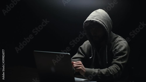 Remote view of unrecognizable hacker man stretching hands and starting to typing on laptop computer keyboard breaking password. Hooded bearded freelancer programmer hacking online site or password.