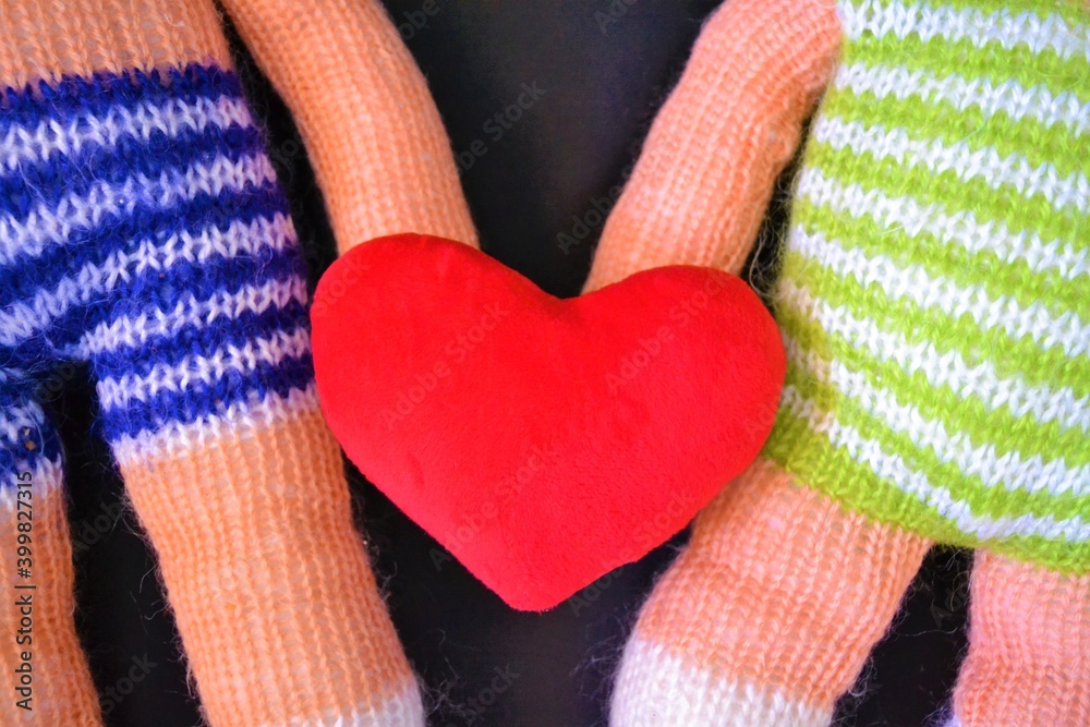 Close up of the bodies of a couple of handmade dolls on a black background with a heart in the middle symbolizing the elove between two people