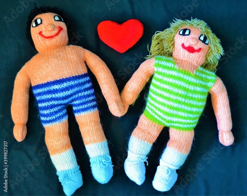 Couple of handmade dolls on a black background with a heart in the middle symbolizing the elove between two people photo