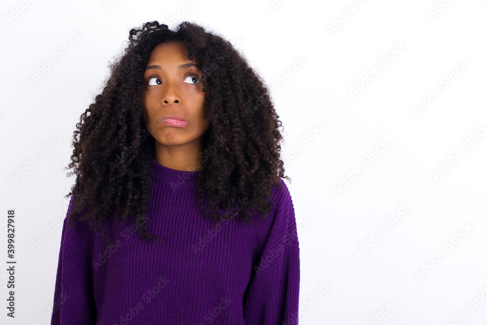 Fototapeta premium Young beautiful African American woman wearing knitted sweater against white wall making grimace and crazy face, screaming out of control, funny lunatic expressing freedom and wild.