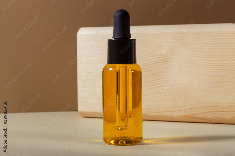 Naklejka premium A glass cosmetic bottle with a dropper on a beige background in bright sunlight. The concept of natural cosmetics, natural essential oil.