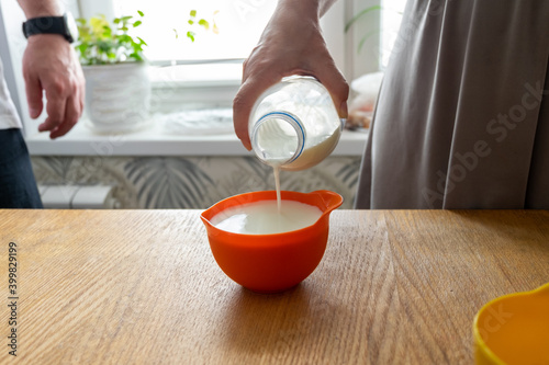 a woman's hand pours milk into a measuring bowl