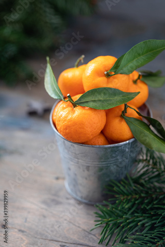 Basket of tangerines on wooden table with Christmas decor and fir tree branches