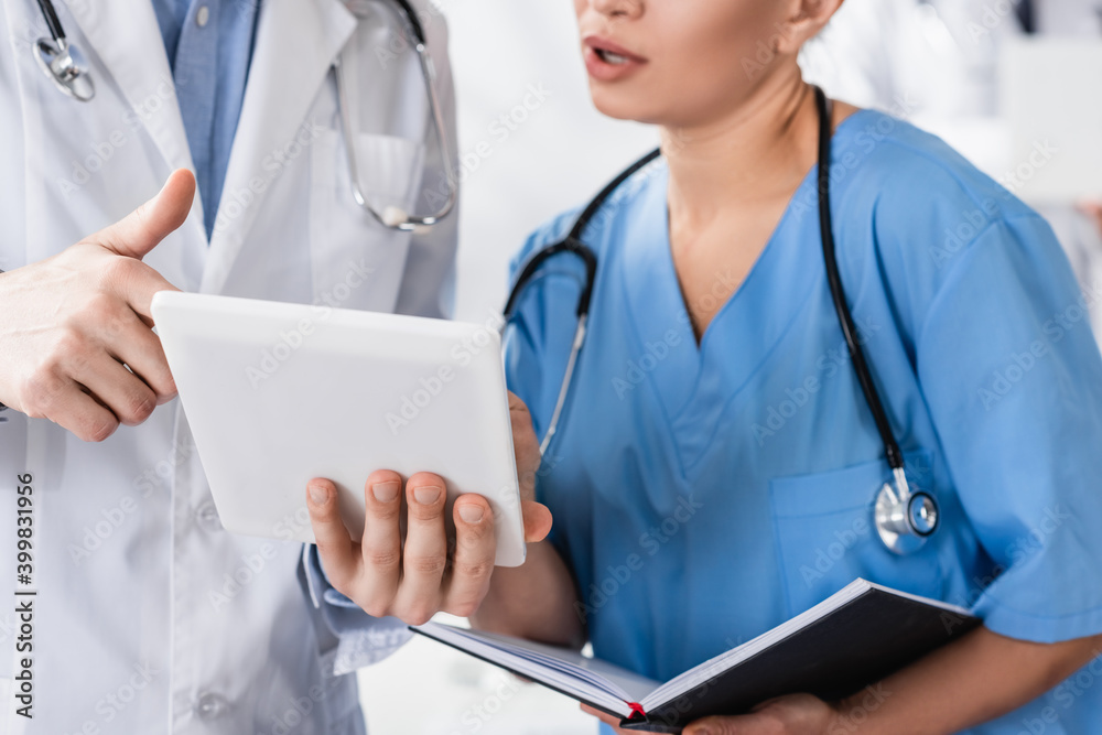 Cropped view of doctor holding digital tablet near nurse with notebook in clinic Cropped view of doctor holding digital tablet near nurse with notebook in clinic