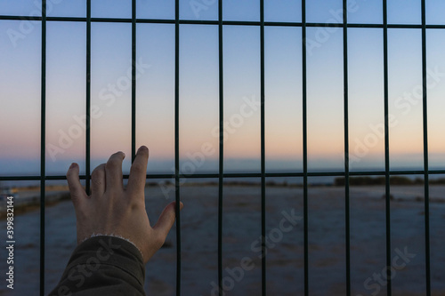 silhouette of a hand from a person watching the sunset behind a fence. photo