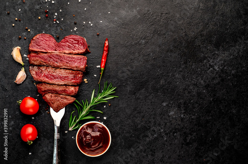 Different degrees of roasting beef steak in heart shape with spices on a meat fork on a stone background with a copy of the space for your text