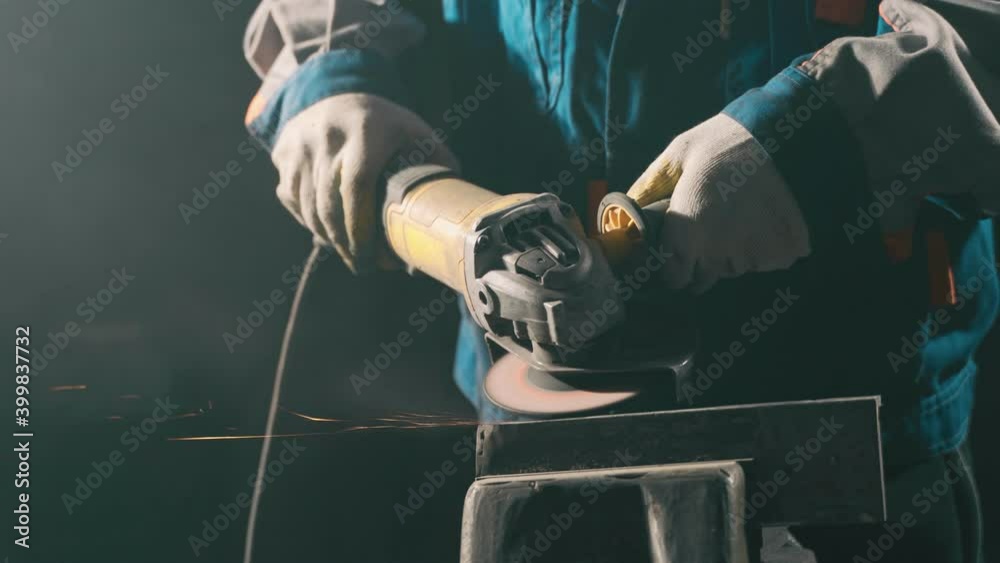 Locksmith in special clothes and goggles works in production. Metal processing with angle grinder. Sparks in metalworking