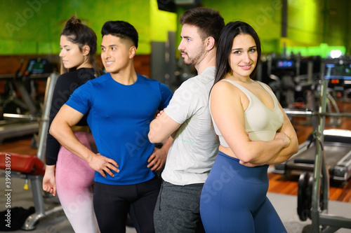 Group of young athletic female and male adults standing together as good friends in gym after workout session. High quality photo
