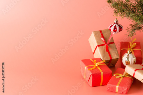 Gifts in beautiful red boxes with gold ribbons under a Christmas tree decorated with glass toys on a pink background. Holiday. New year and Christmas. Banner. Copy space © garmashevanatali