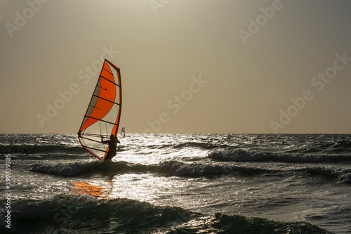 Surfer balances on a windsurf board at sunset. Windsurfing, sailing, water sports, extreme sports.