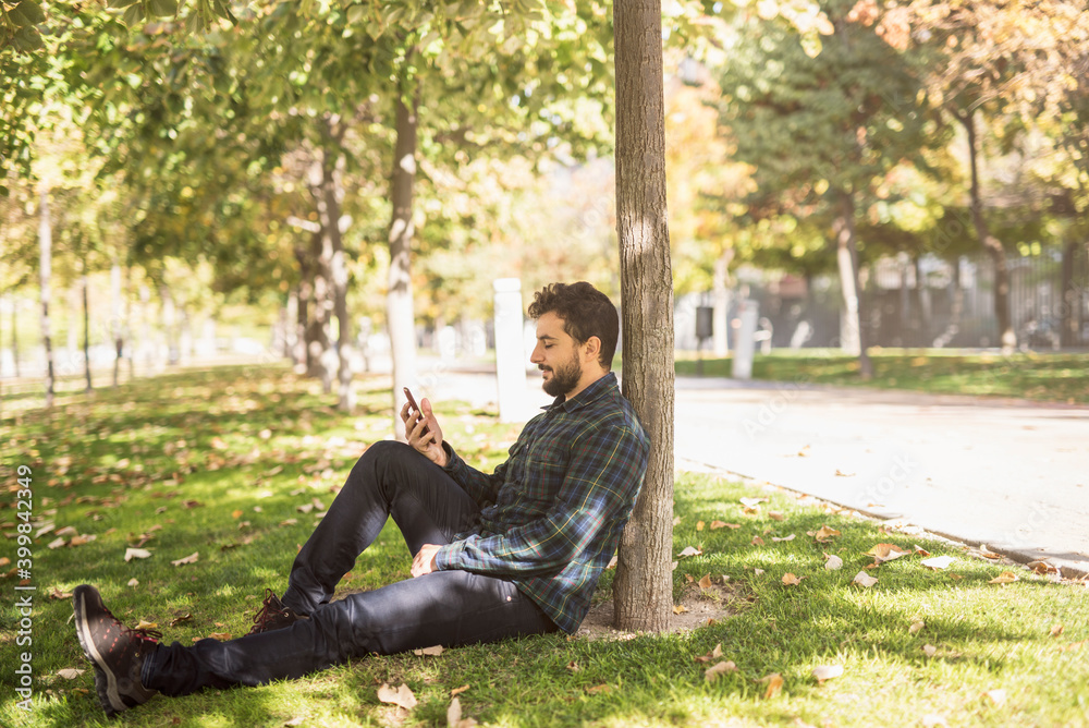Obraz premium Bearded man touching phone sitting in park.