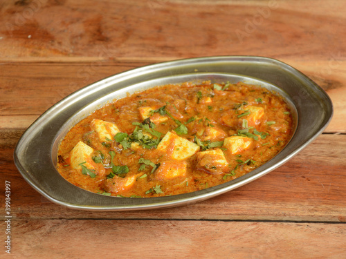 Paneer Butter Masala or Cheese Cottage Curry, served over a rustic wooden background, selective focus