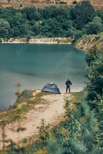 Man standing next to a tent with hands on hips and looking at beautiful untouched nature.