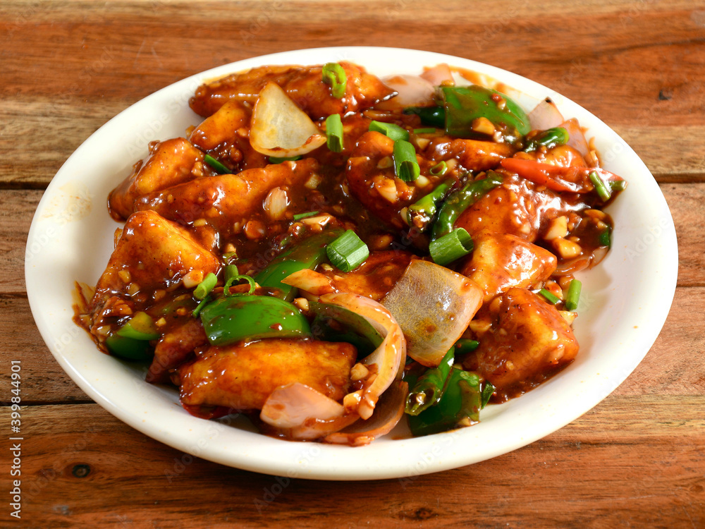 Paneer chilli is Indo Chinese cuisine dish, Paneer cubes tossed with tomatoes, onions, spring onions, chilli sauce. served over a rustic wooden background, selective focus