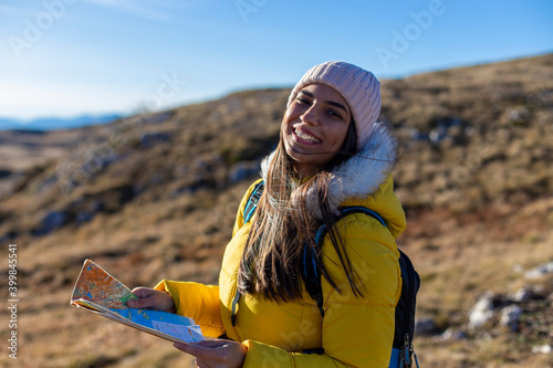 Portrait of smiling woman hiking and holding a geographical map at the top of the mountain.