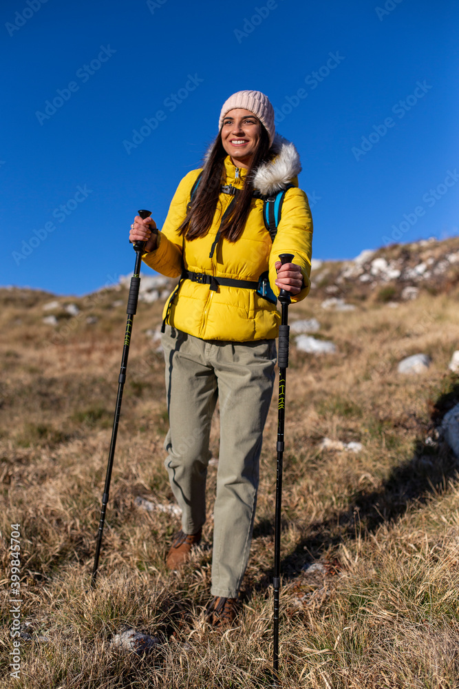 A smiling woman is hiking at the top of the mountain. 