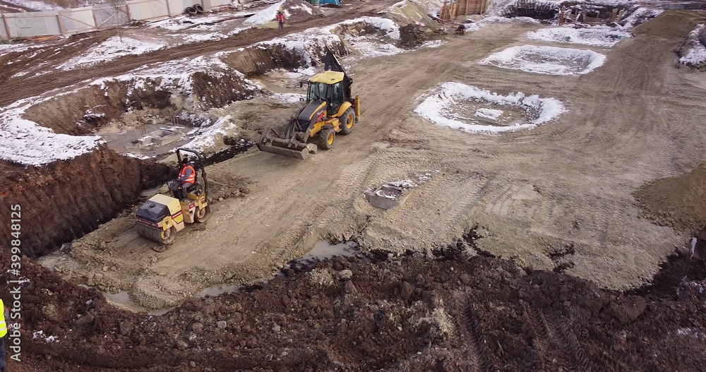 Obraz premium Aerial view of heavy machinery, tractor transporting land, construction preparation. The skating rink compacts the ground. Start of construction of the building flick.