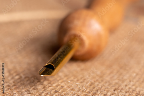 Macro photography of a golden punch needle with wooden handle on a piece of jute fabric. Focus on the tip of the needle and blurred background.