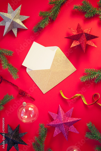 Spruce branches, decorative balls with stars on red background with envelope and paper card note. Christmas composition. Happy New Year. Space for text. Flat lay, top view