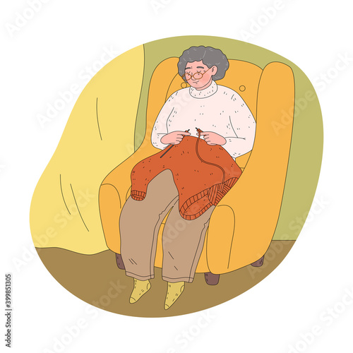 Grandmother in glasses sitting in armchair at home and knitting warm sweater