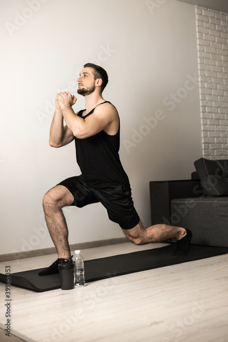 Athletic man doing lunge forward. Sport at home concept. Strong man stretching legs before workout. Healthcare concept. Male sportsman in black sportswear. Fitness or yoga.