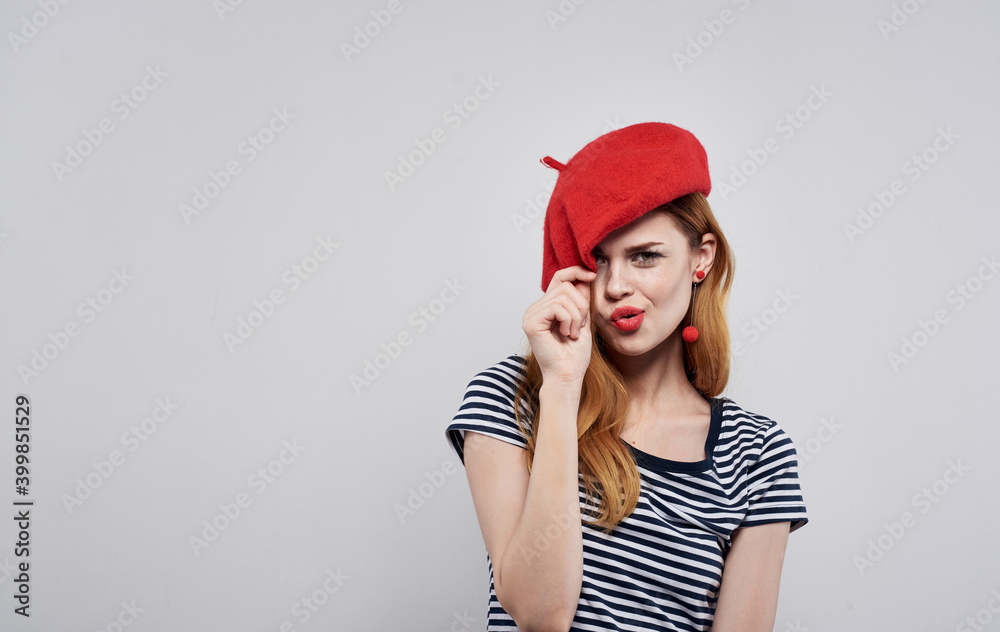 Woman in striped t-shirt touches red hat on her head light background cropped view Woman in striped t-shirt touches red hat on her head light background cropped view