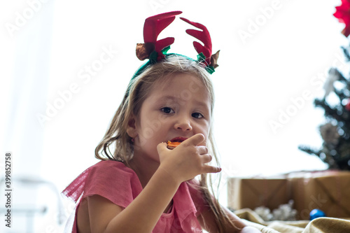 Cute little girl wearing reindeer headband and eating gingerbread cookies and biscuits. Merry Christmas and happy holidays