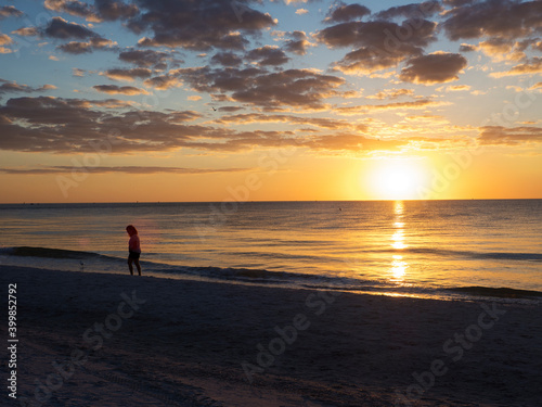 Young woman walking on a Gulf of Mexico beach at St. Pete Beach, Florida at sunset with a dramatic orange sunlit sky.
