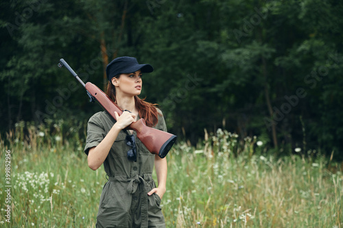 Woman on nature gun on shoulder green jumpsuit travel fresh air green leaves 