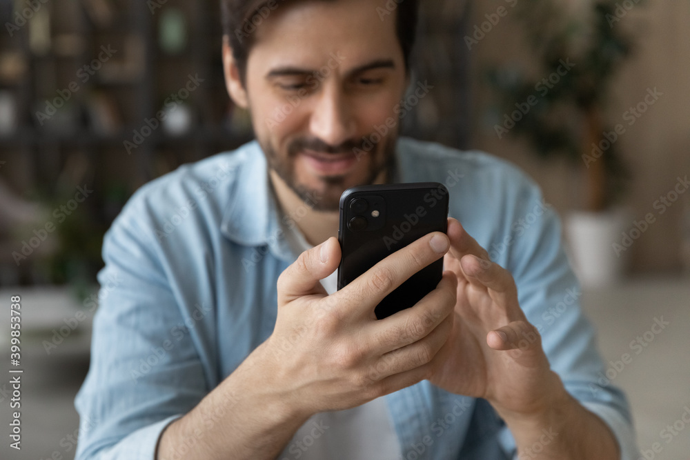 Crop close up of happy millennial male look at cellphone screen browse surf wireless internet on gadget. Smiling young Caucasian man use smartphone texting or messaging online on device. Crop close up of happy millennial male look at cellphone screen browse surf wireless internet on gadget. Smiling young Caucasian man use smartphone texting or messaging online on device.