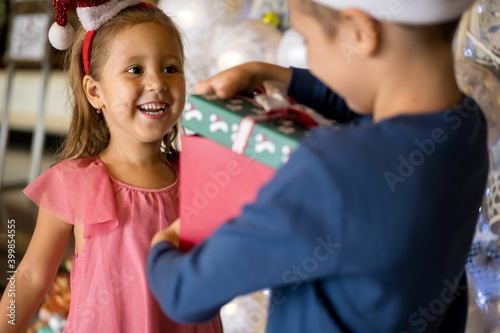 Two adorable little children: brother and sister are exchanging gifts and presents near Christmas tree. Merry Christmas and happy holidays