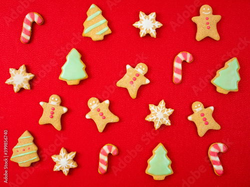 Variety shapes of Christmas cookies: gingerbread man with surgical protective mask, Christmas tree, snowflake, candy stick. Homemade bakery on red background. Flat lay. Christmas coronavirus.