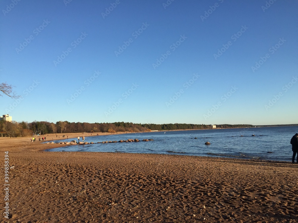 Autumn evening the sun is approaching the horizon. Blue water of the Gulf of Finland, small waves on the water. In the distance, the outlines of buildings on the shore are visible. Light blue sky abov