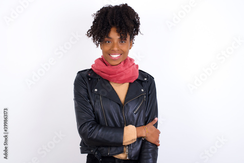 Young beautiful hipster African American woman wearing biker jacket against white wall laughing.