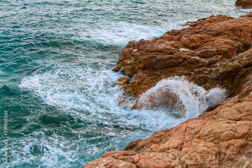 Sea waves with splashes hit the coastal rocks