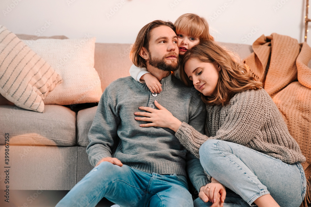 Parents hug little daughter while sitting in the room decorated for christmas