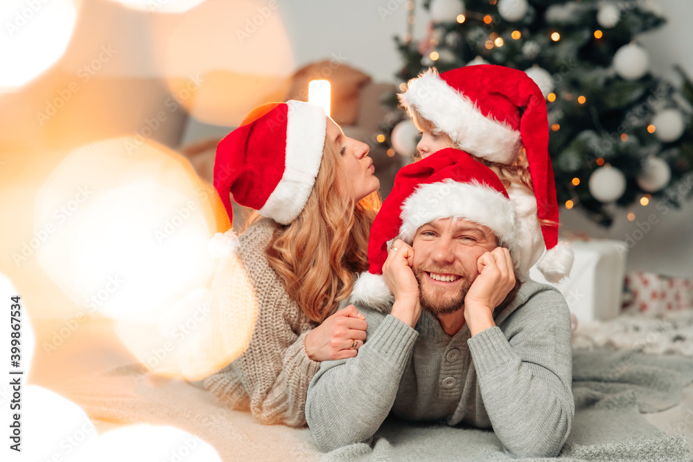 Family in santa claus hats lie on the floor of christmas decorated room Family in santa claus hats lie on the floor of christmas decorated room