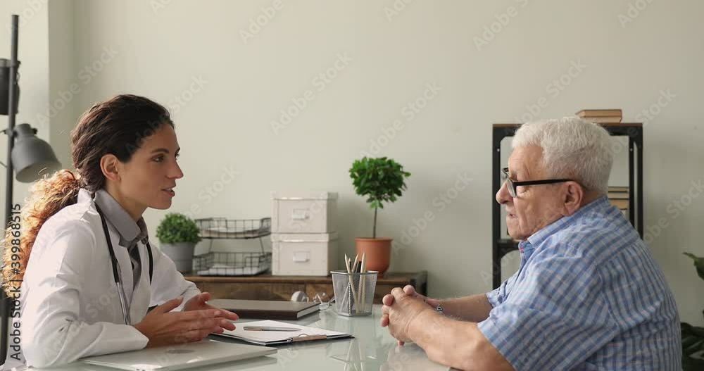 Older male patient visiting physician tell about health complaints. Female medical practitioner ask questions talks to mature patient filling disease history form, provide help and prescribe treatment Older male patient visiting physician tell about health complaints. Female medical practitioner ask questions talks to mature patient filling disease history form, provide help and prescribe treatment