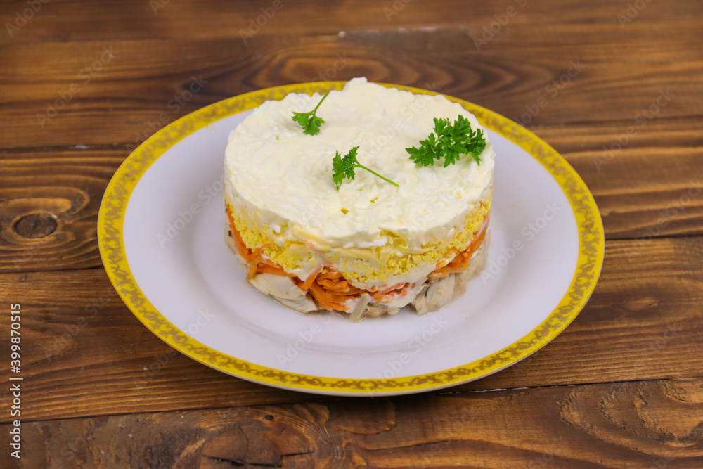 Tasty layered salad with chicken, carrot, eggs, cheese and mayonnaise on wooden table