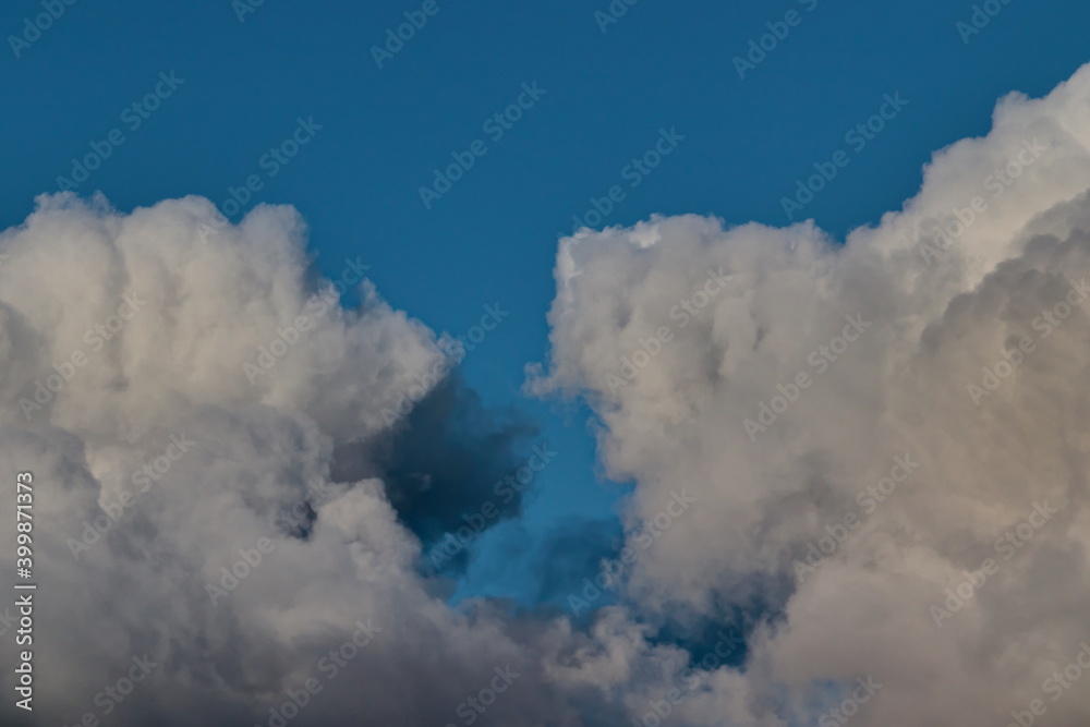 two large cumulus clouds shaded with gray floating nearby under a blue sky.