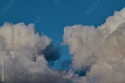 two large cumulus clouds shaded with gray floating nearby under a blue sky.