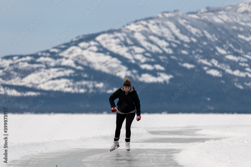 Woman skating on frozen lake in northern Canada with huge mountains in the background surrounded by snow, snow capped and glassy ice on lakes surface. Woman skating on frozen lake in northern Canada with huge mountains in the background surrounded by snow, snow capped and glassy ice on lakes surface.