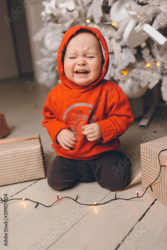 Sad child at the New Year tree. Upset little boy at christmas.